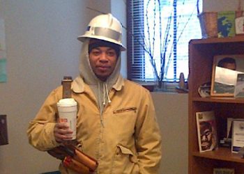 Person wearing a white hardhat inside while holding a coffee