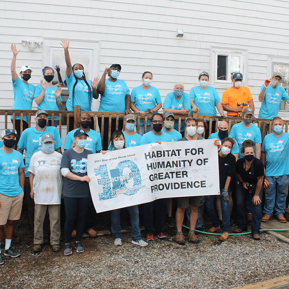 A group of people wearing blue shirts holding up a sign that says "Habitat for Humanity of Greater Providence"