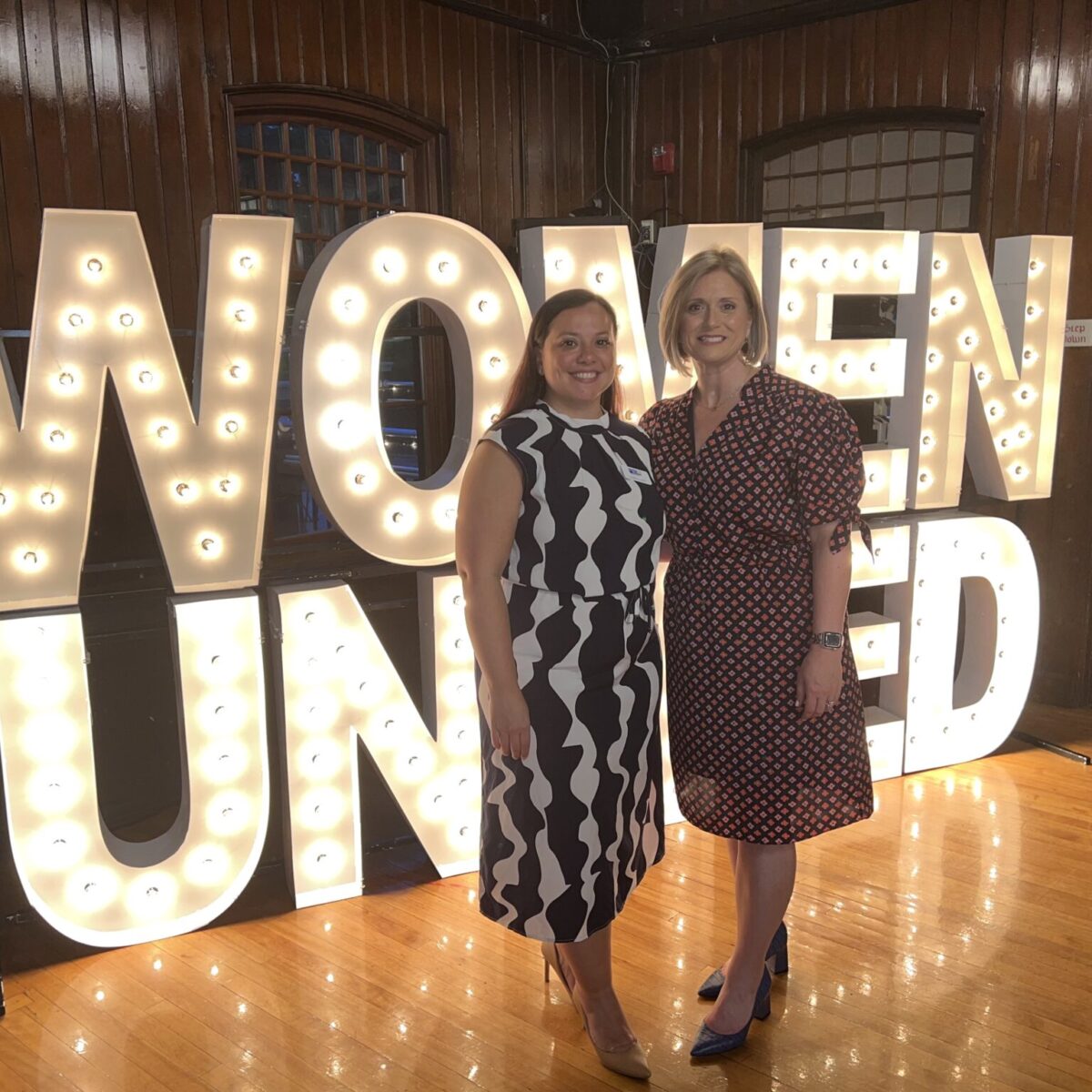 United Way of Rhode Island’s Karen Alzate and Cortney Nicolato pose in front of marquee letters.
