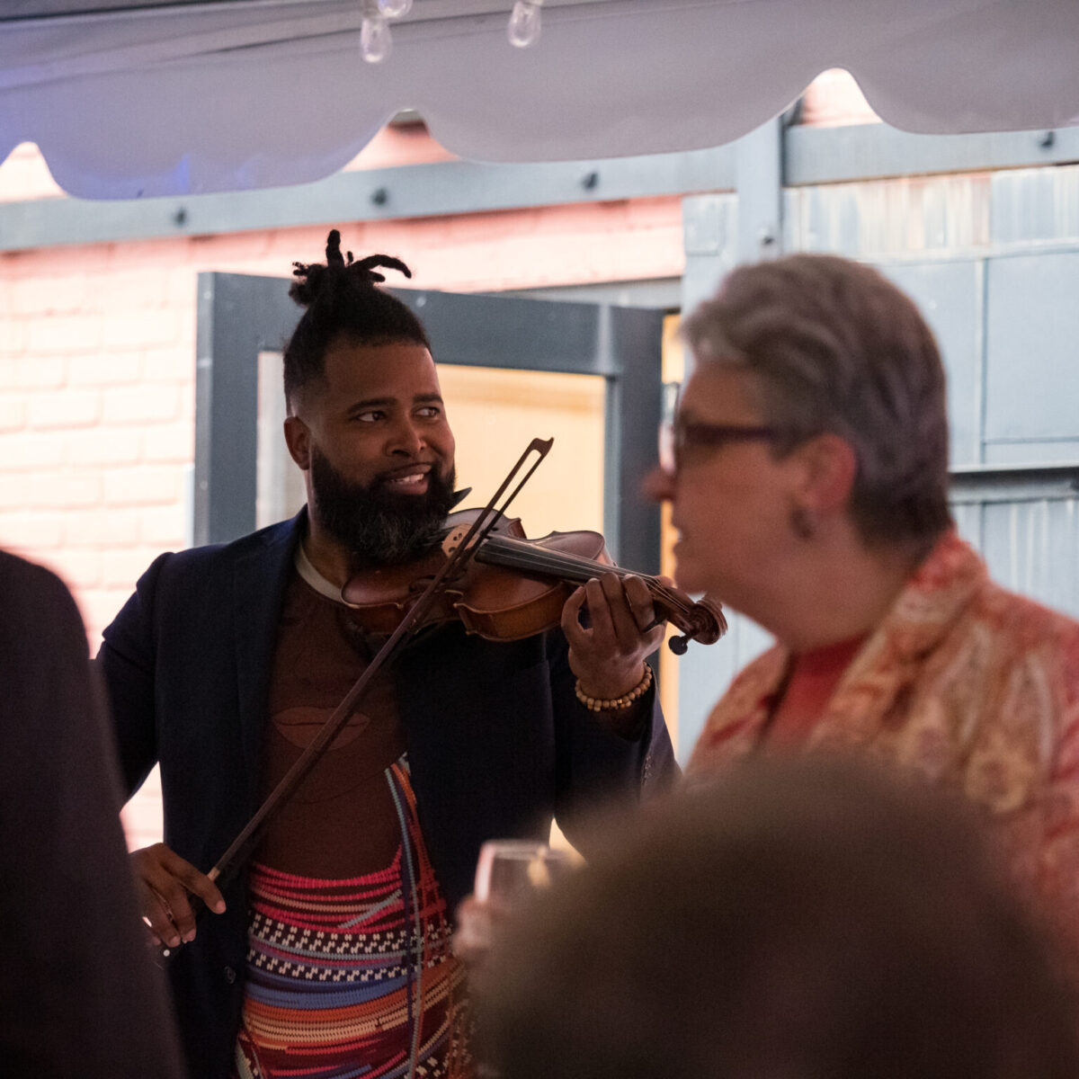 Musician Big Lux smiles while playing violin among attendees.