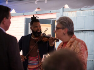 Musician Big Lux smiles while playing violin among attendees.