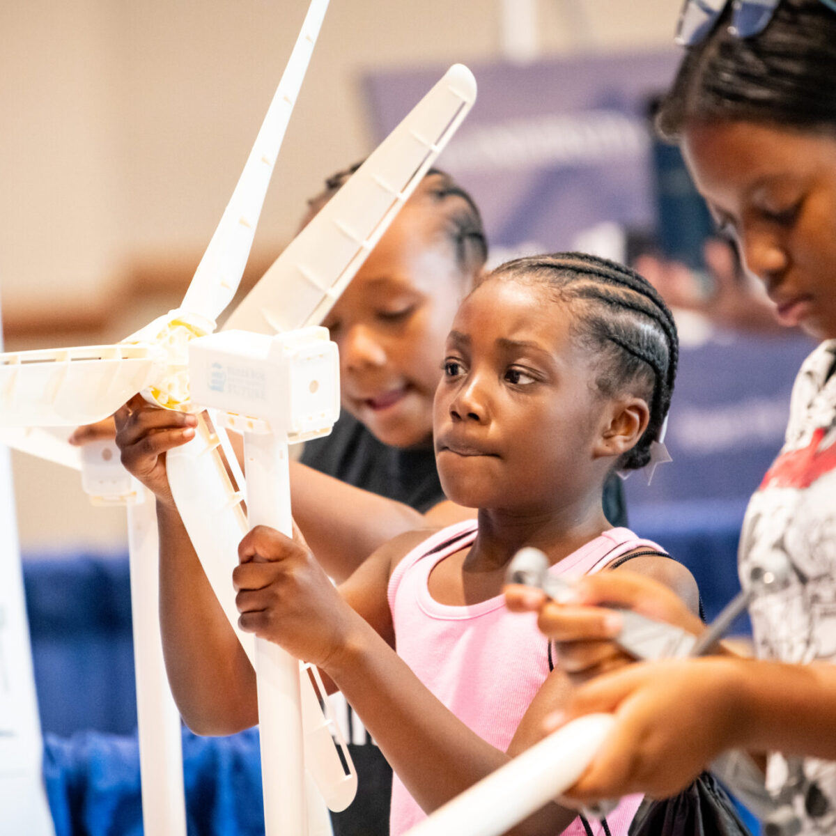 Three young children work on a white wind toy