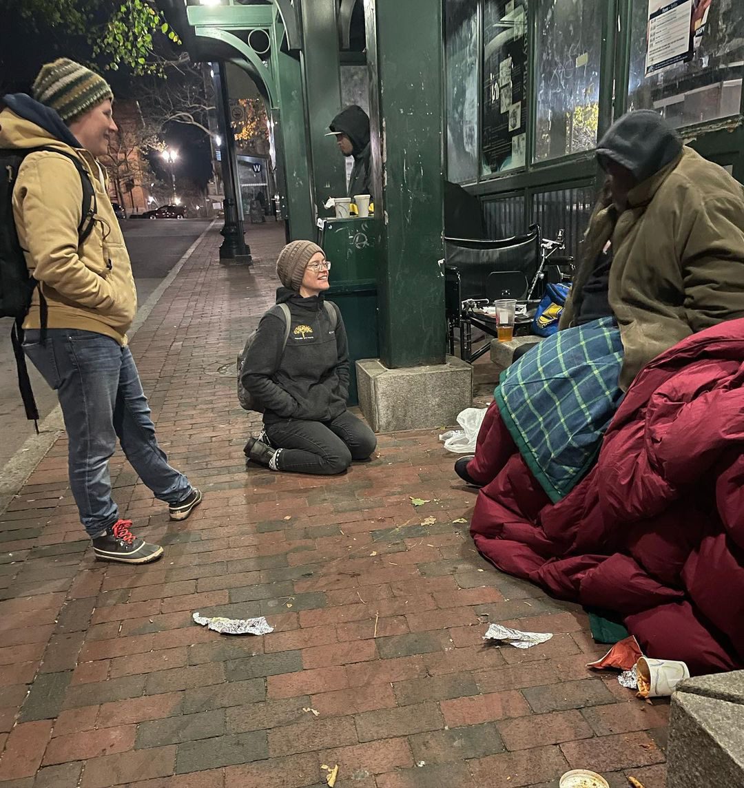 Group of people sitting outside on the street wearing warm clothing