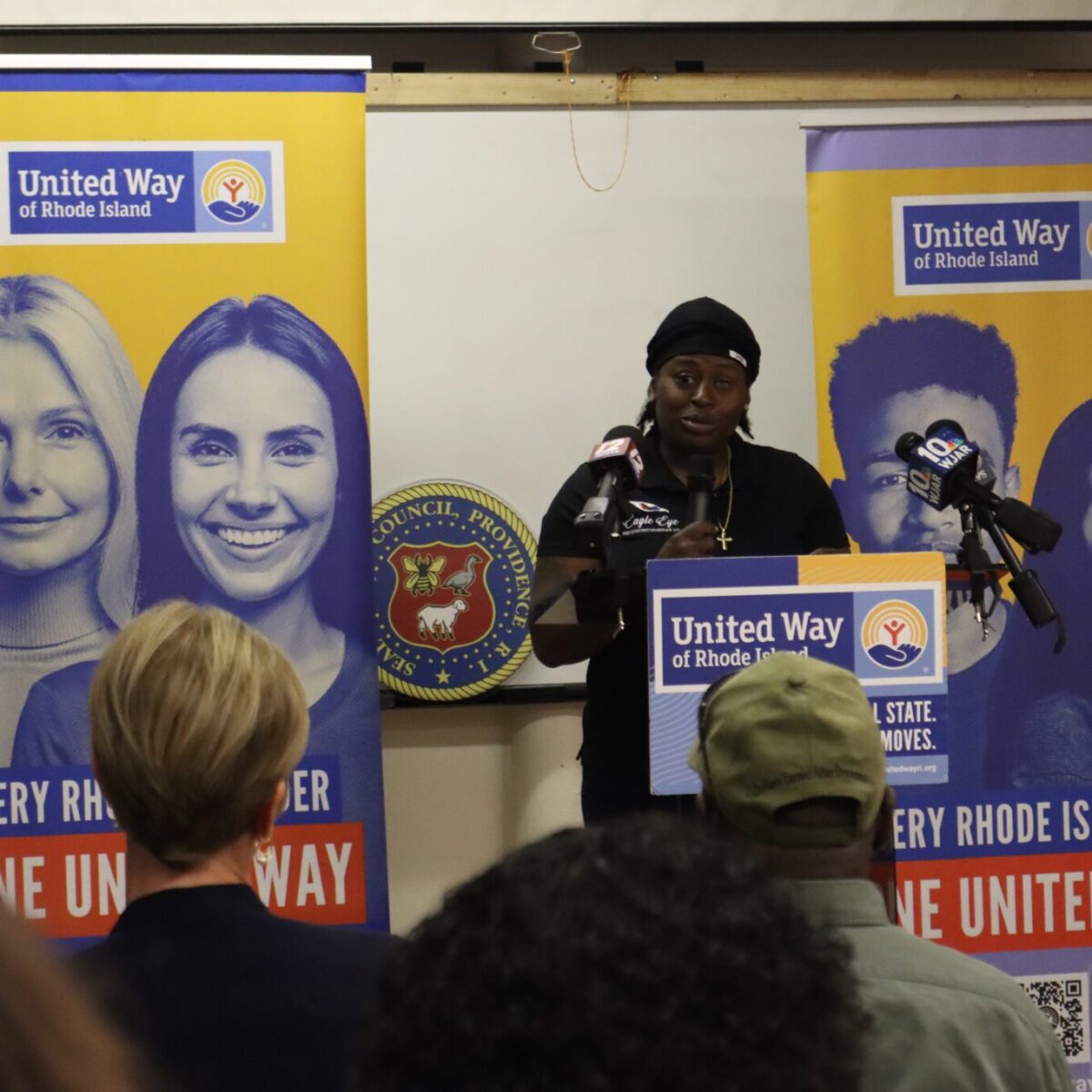 A Black person wearing black clothing and speaking from a podium.
