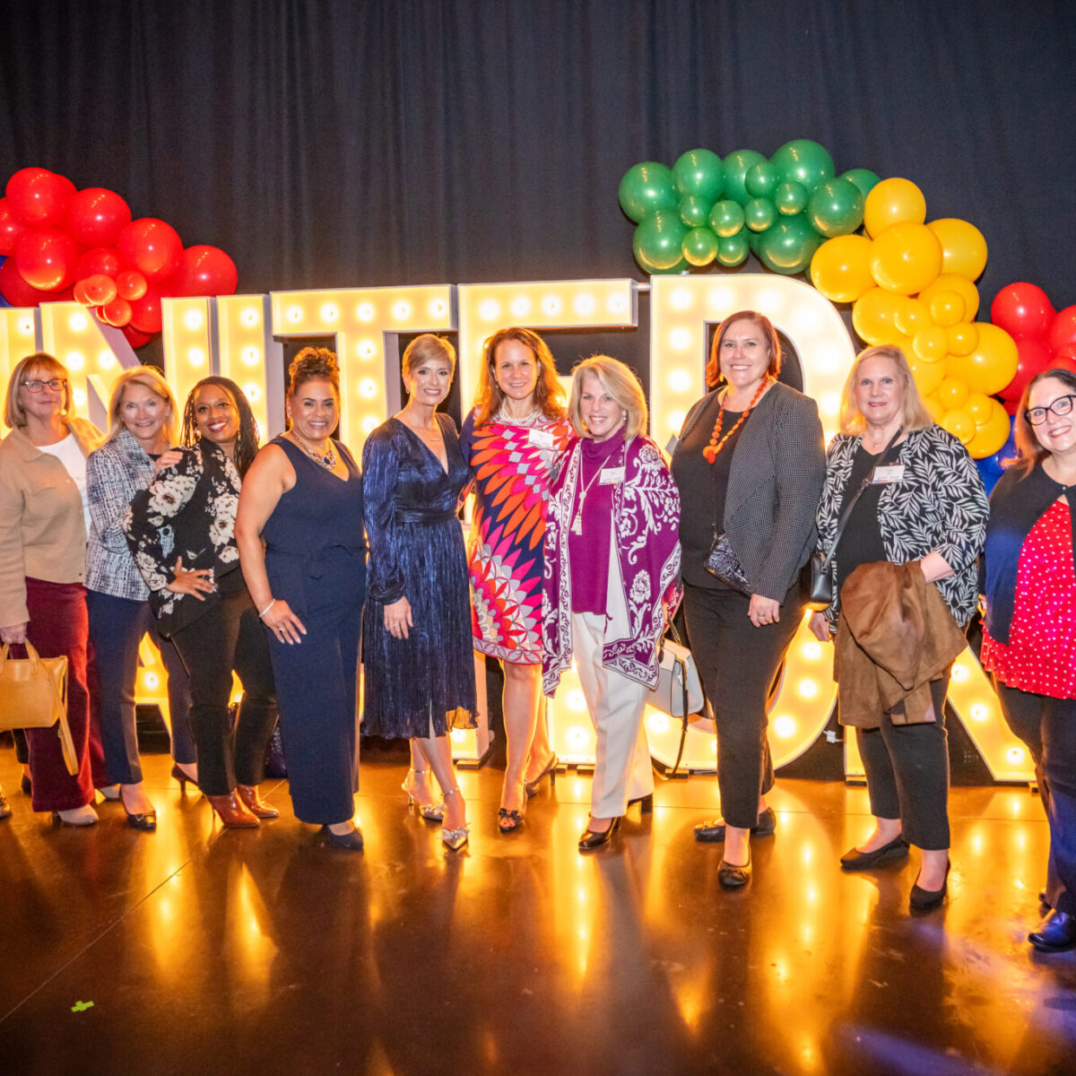 Members of United Way of Rhode Island's Women United posing with green, yellow, blue, and red balloons.