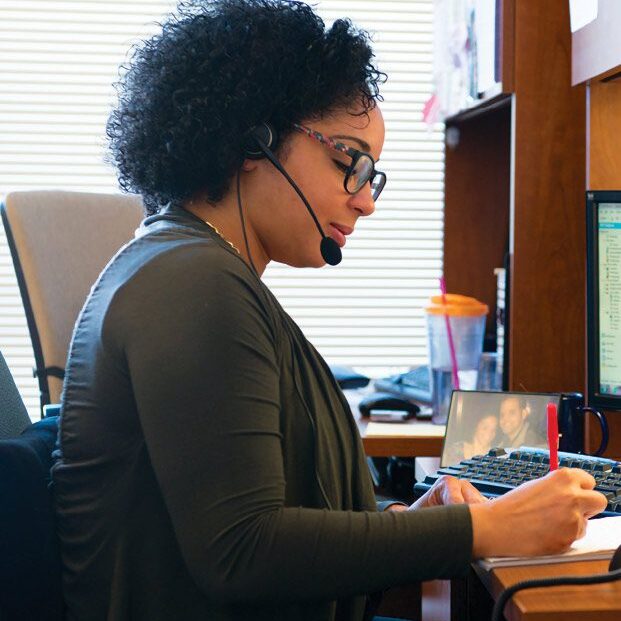 computer A person sitting at a desk while wearing a microphone ear piece